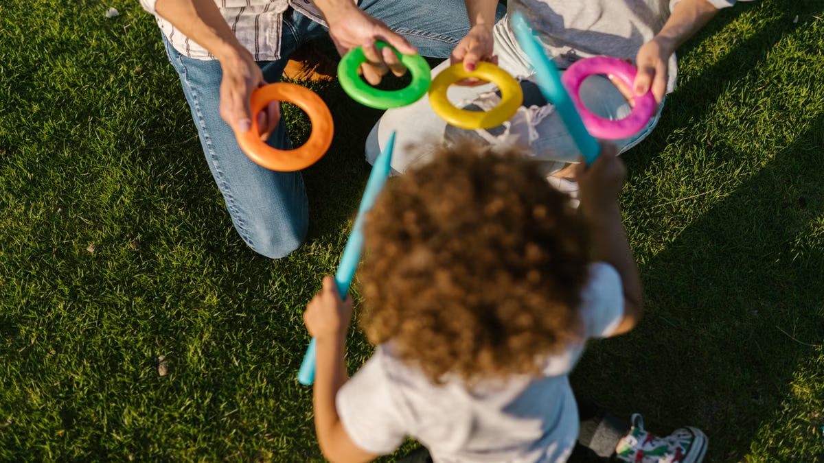 Child playing with colorful rings outdoors on a sunny day with adults.